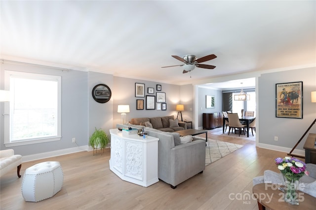 living room featuring crown molding, light wood-style flooring, ceiling fan, and baseboards