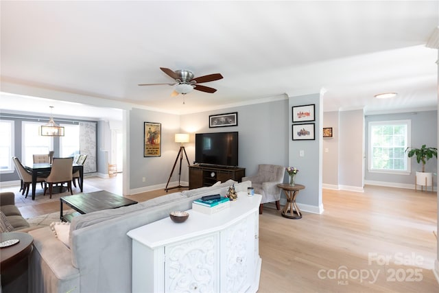 living area featuring crown molding, ceiling fan, baseboards, and light wood-type flooring