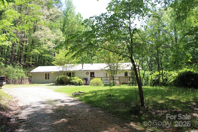 single story home with gravel driveway and a forest view