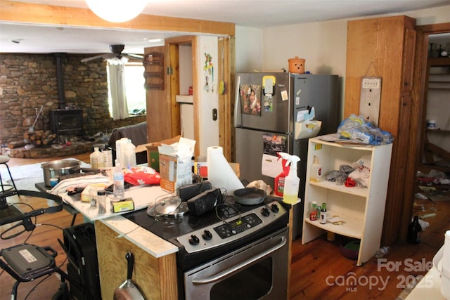 kitchen with a ceiling fan, a wood stove, appliances with stainless steel finishes, and wood finished floors