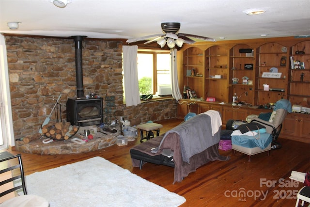 living room featuring a ceiling fan, a wood stove, and hardwood / wood-style flooring