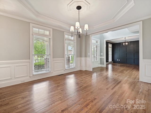 unfurnished dining area featuring crown molding, a raised ceiling, a decorative wall, and a chandelier