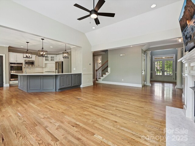 unfurnished living room with a high end fireplace, vaulted ceiling, stairway, ceiling fan with notable chandelier, and light wood-style flooring