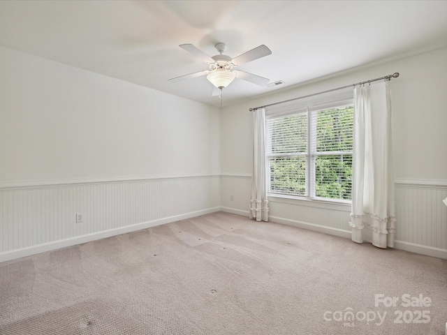 spare room featuring visible vents, a ceiling fan, wainscoting, and carpet