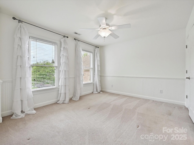 carpeted empty room featuring ceiling fan, visible vents, and wainscoting
