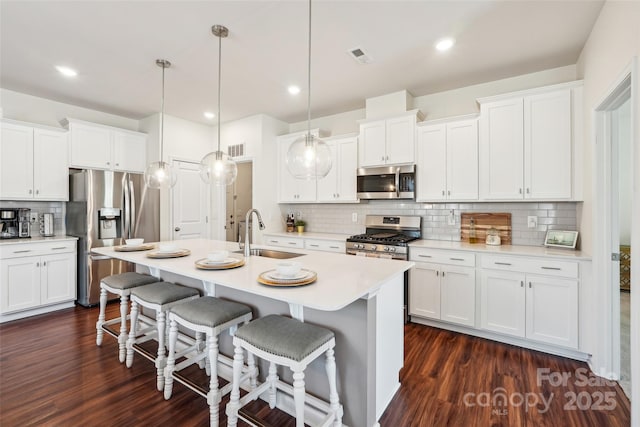 kitchen with a breakfast bar, a sink, light countertops, stainless steel appliances, and tasteful backsplash