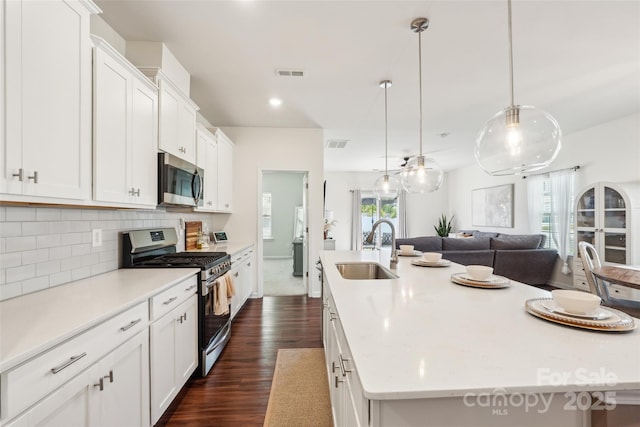 kitchen with a sink, stainless steel appliances, a large island with sink, visible vents, and dark wood-style floors