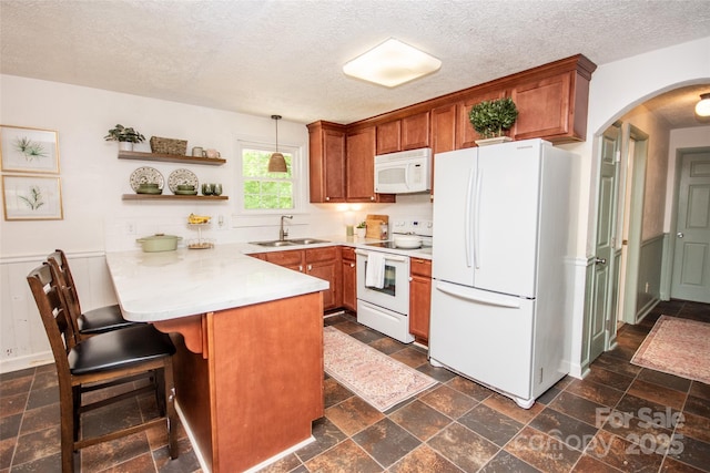 kitchen with brown cabinetry, a peninsula, white appliances, arched walkways, and a sink