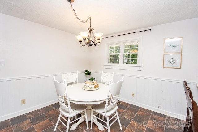 dining space featuring stone finish floor, baseboards, wainscoting, and a notable chandelier