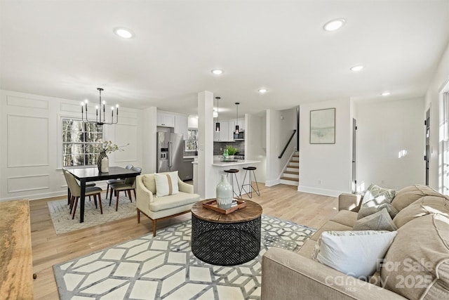 living area featuring baseboards, stairway, recessed lighting, light wood finished floors, and a notable chandelier