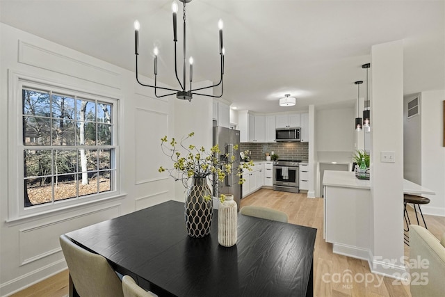 dining area featuring baseboards, an inviting chandelier, visible vents, and light wood-type flooring