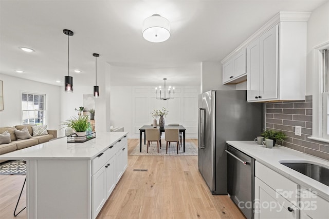 kitchen with decorative backsplash, appliances with stainless steel finishes, light wood-type flooring, white cabinets, and a notable chandelier