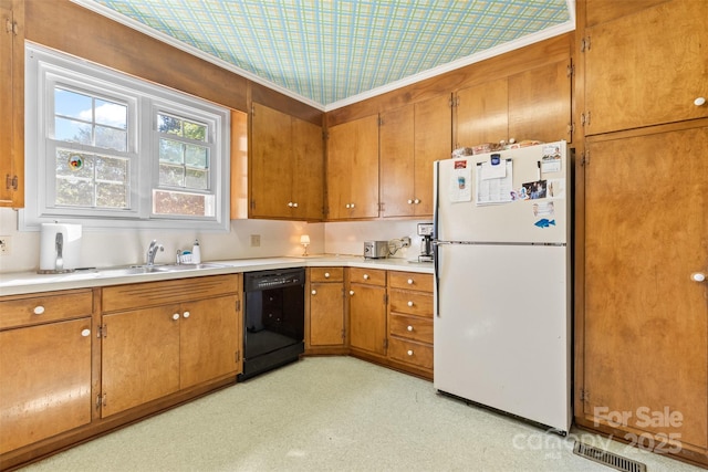 kitchen featuring brown cabinets, a sink, light countertops, freestanding refrigerator, and black dishwasher