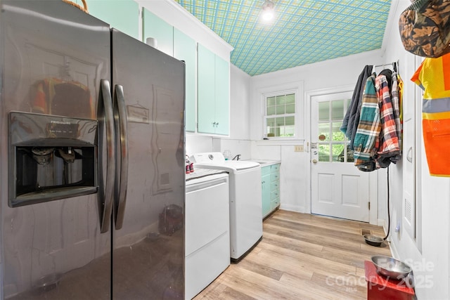 clothes washing area featuring light wood-style floors, washer and clothes dryer, and cabinet space