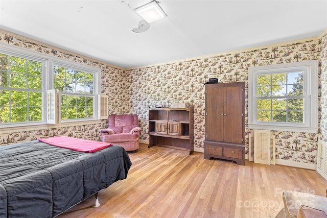 bedroom featuring baseboards, wallpapered walls, multiple windows, and wood finished floors