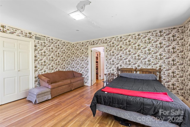 bedroom with wallpapered walls, ornamental molding, and wood finished floors