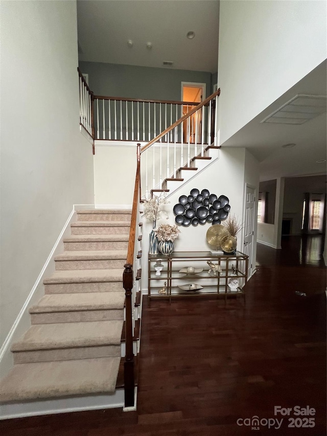 staircase with baseboards, a high ceiling, and wood finished floors