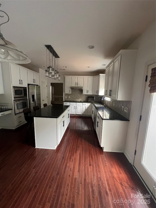 kitchen featuring dark wood-style flooring, dark countertops, a center island, a sink, and stainless steel appliances