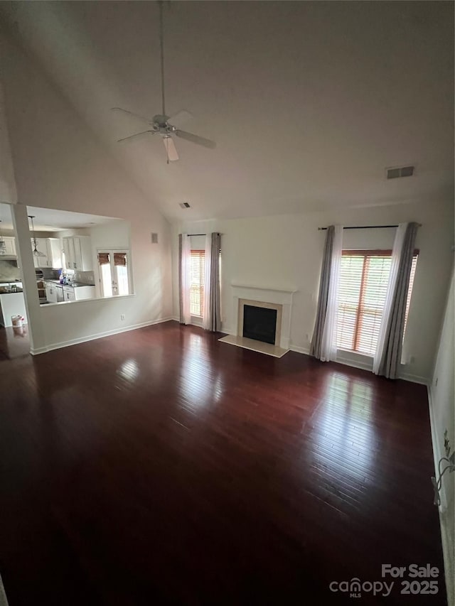 unfurnished living room with a healthy amount of sunlight, a ceiling fan, dark wood finished floors, and visible vents