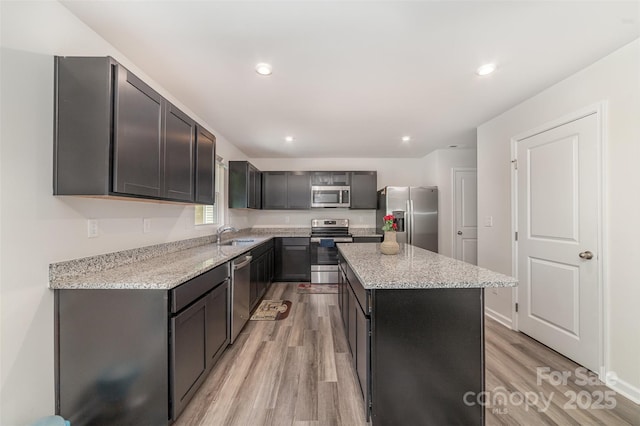 kitchen with light stone countertops, appliances with stainless steel finishes, light wood-style floors, recessed lighting, and a kitchen island