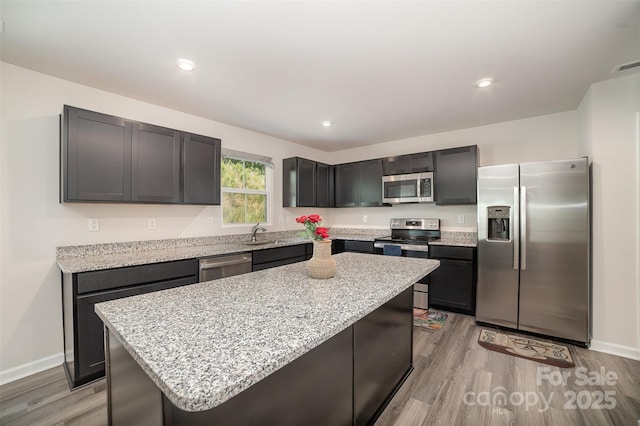 kitchen featuring baseboards, light wood-style floors, a center island, light stone counters, and appliances with stainless steel finishes
