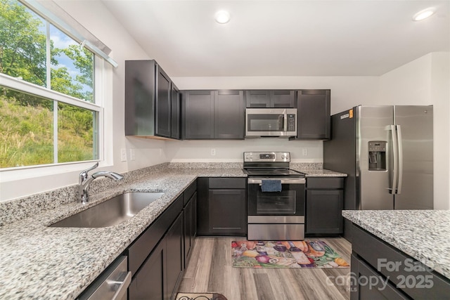 kitchen featuring light stone counters, appliances with stainless steel finishes, a sink, recessed lighting, and light wood-type flooring