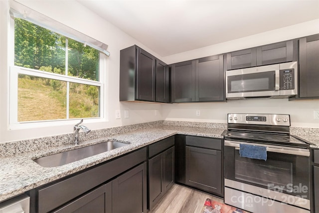 kitchen with stainless steel appliances, light stone countertops, a sink, and light wood-type flooring