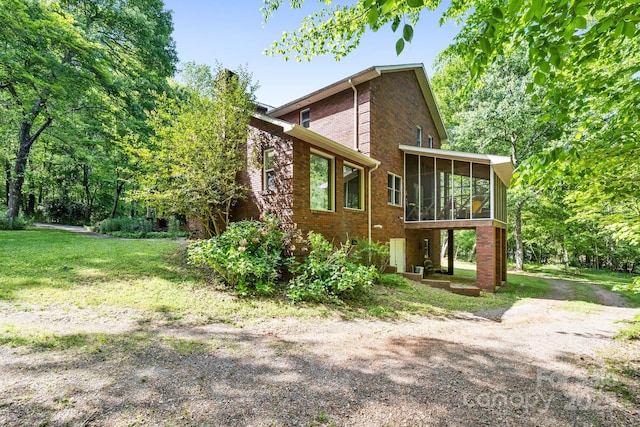 exterior space with a sunroom, a lawn, and brick siding
