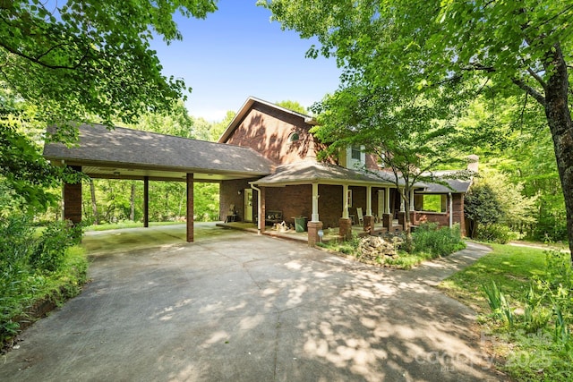 view of front of home with brick siding, a carport, a chimney, concrete driveway, and covered porch