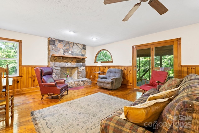 living area featuring wooden walls, a textured ceiling, a wainscoted wall, a ceiling fan, and hardwood / wood-style flooring