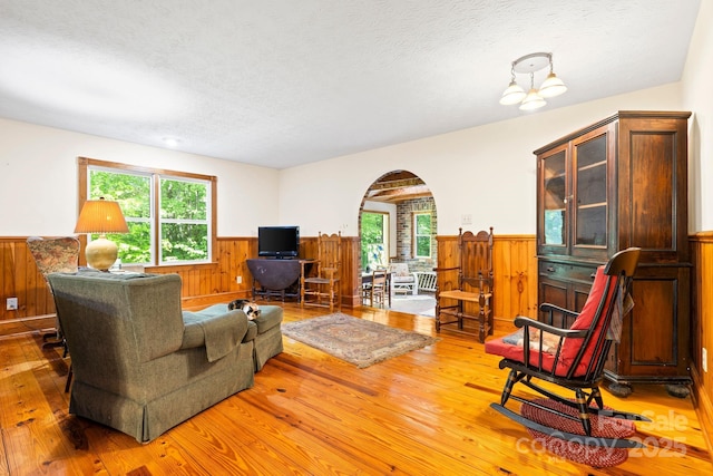 living area featuring light wood-style floors, a wainscoted wall, arched walkways, and a healthy amount of sunlight