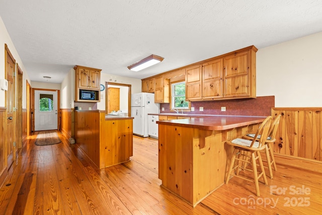 kitchen featuring freestanding refrigerator, a peninsula, black microwave, light wood-style floors, and a wainscoted wall