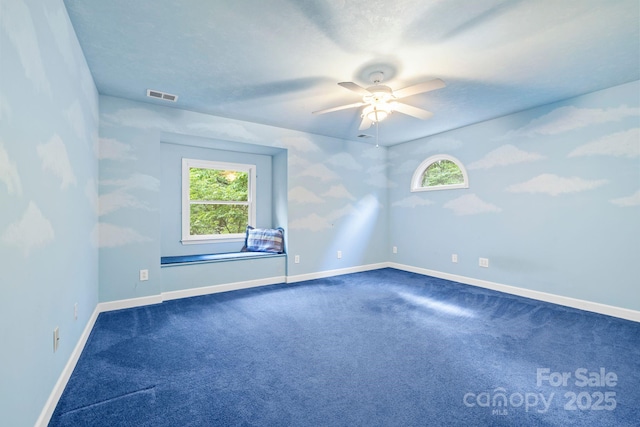 spare room featuring baseboards, ceiling fan, dark colored carpet, and visible vents