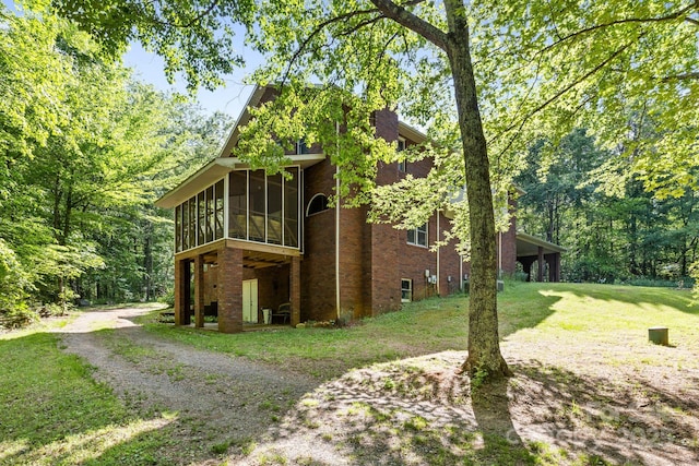 view of property exterior featuring a yard, brick siding, a sunroom, and dirt driveway