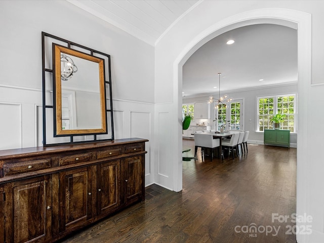 hall featuring a decorative wall, arched walkways, a chandelier, dark wood finished floors, and a wealth of natural light
