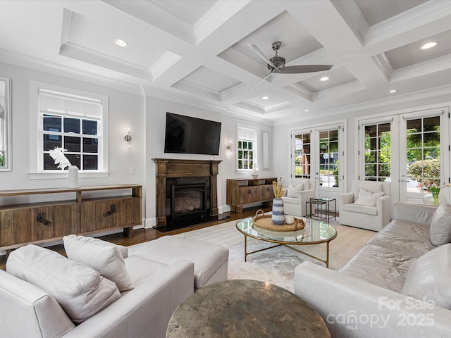 living area with french doors, a ceiling fan, a fireplace with flush hearth, wood finished floors, and coffered ceiling