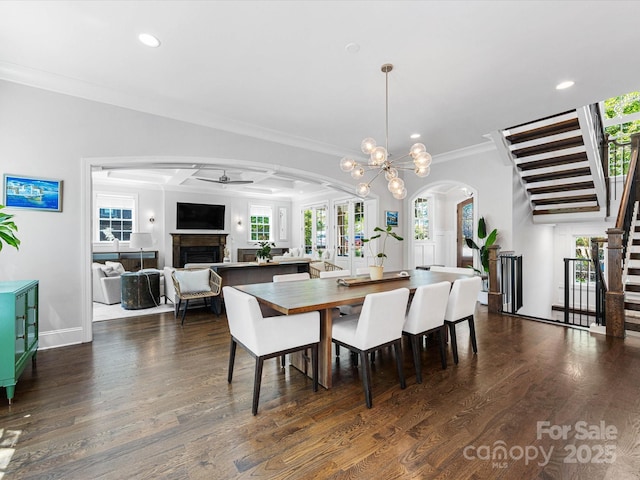 dining space with a ceiling fan, crown molding, arched walkways, a fireplace, and stairs