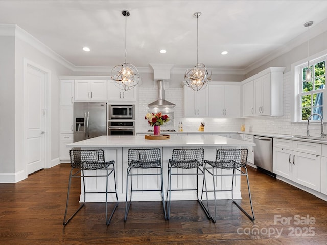 kitchen with wall chimney range hood, a sink, light countertops, stainless steel appliances, and a kitchen island