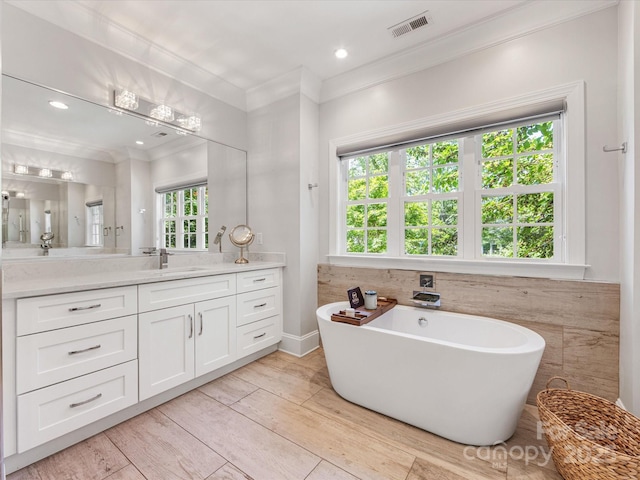 bathroom featuring vanity, wood finished floors, visible vents, ornamental molding, and a soaking tub