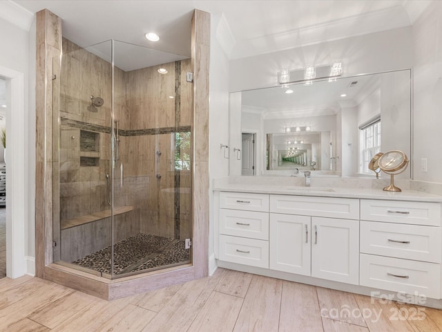 full bathroom featuring wood finished floors, ornamental molding, a shower stall, and vanity