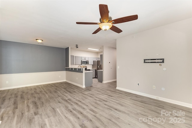 unfurnished living room featuring ceiling fan, light wood-style flooring, and baseboards