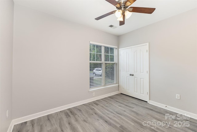 unfurnished bedroom featuring wood finished floors, a closet, baseboards, and ceiling fan