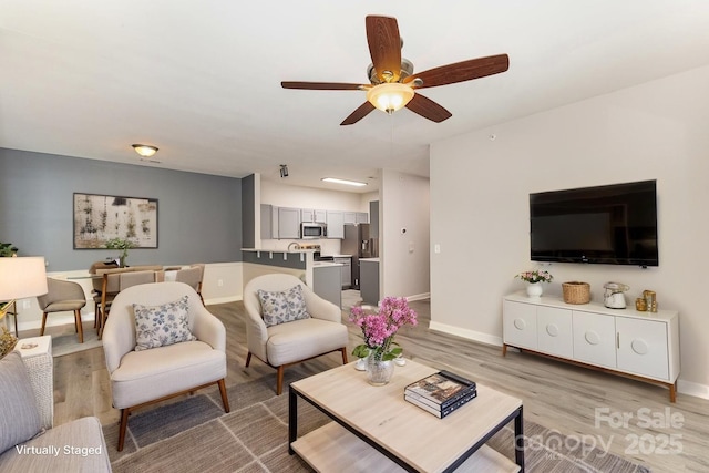 living room featuring a ceiling fan, baseboards, and light wood finished floors