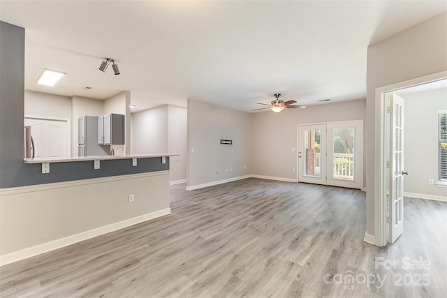 unfurnished living room featuring light wood-type flooring, a ceiling fan, and baseboards