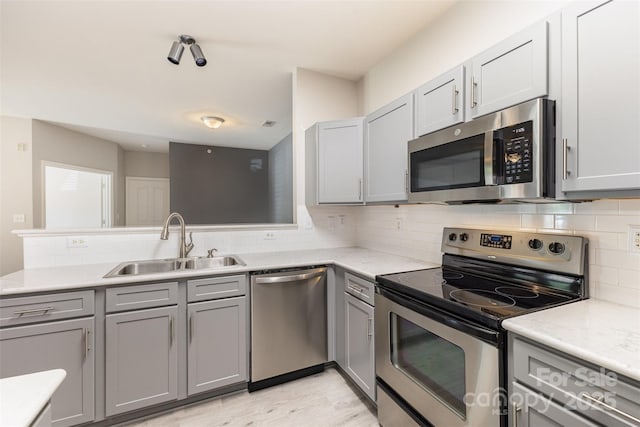 kitchen featuring appliances with stainless steel finishes, a sink, gray cabinetry, tasteful backsplash, and a peninsula