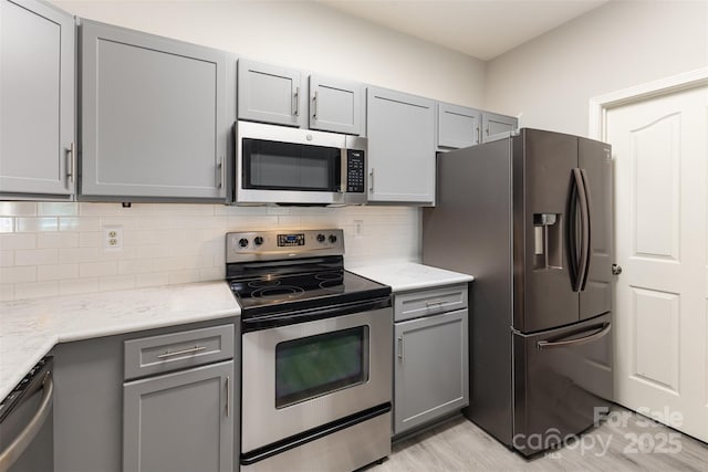 kitchen featuring stainless steel appliances, gray cabinets, backsplash, and light wood-style flooring