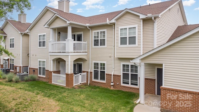back of property with a balcony, brick siding, a yard, and a chimney