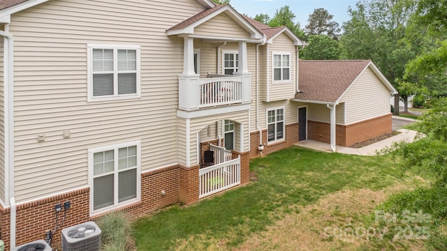 back of property with brick siding, central AC unit, a balcony, and a lawn