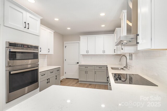 1208 Fordham Rd, Charlotte, NC 28208 - kitchen with a sink, black electric cooktop, stainless steel double oven, wall chimney range hood, and tasteful backsplash