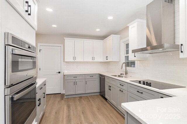 1208 Fordham Rd, Charlotte, NC 28208 - kitchen featuring wall chimney range hood, a sink, appliances with stainless steel finishes, light wood finished floors, and light countertops